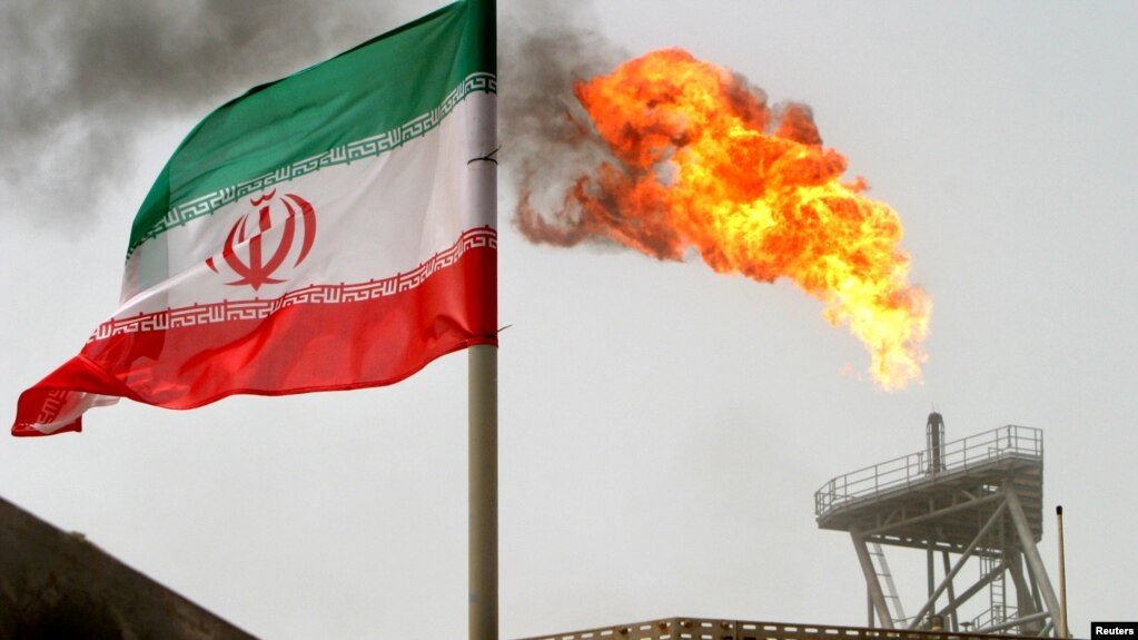 FILE - A gas flare on an oil production platform in the Soroush oil fields is seen alongside an Iranian flag in the Persian Gulf, Iran, July 25, 2005.