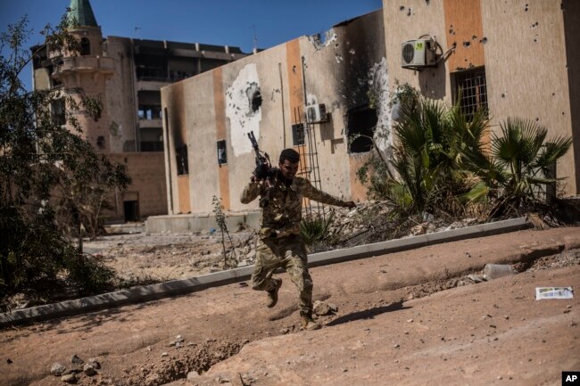 FILE - A fighter of the Libyan forces, affiliated with the Tripoli government, runs for cover while fighting against Islamic State positions in Sirte, Libya, Sept. 22, 2016.