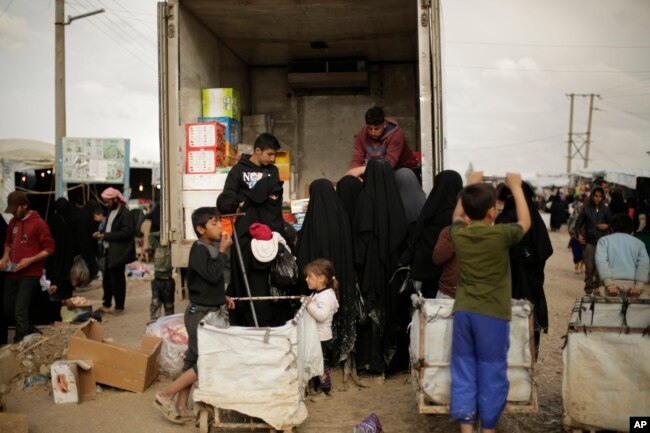 FILE - In this March 31, 2019, photo, women purchase goods from the back of a truck in the marketplace at al-Hol camp, near Hasakah, Syria. Al-Hol camp is home to thousands of people who streamed out of the Islamic State group’s last strongholds.