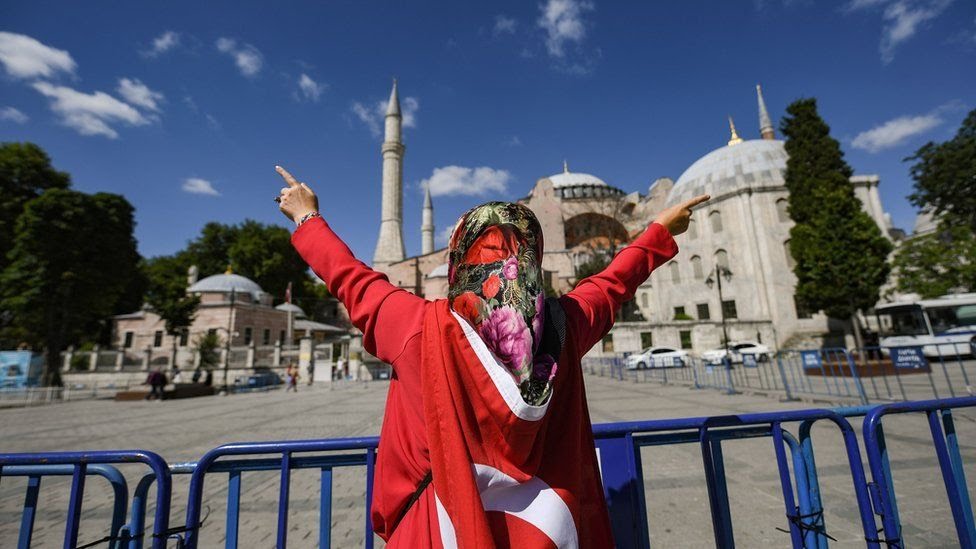 A woman wrapped in a Turkish national flag gestures outside the Hagia Sophia museum on July 10, 2020 in Istanbul as people gather to celebrate after a top Turkish court revoked the sixth-century Hagia Sophias status as a museum, clearing the way for it to be turned back into a mosque
